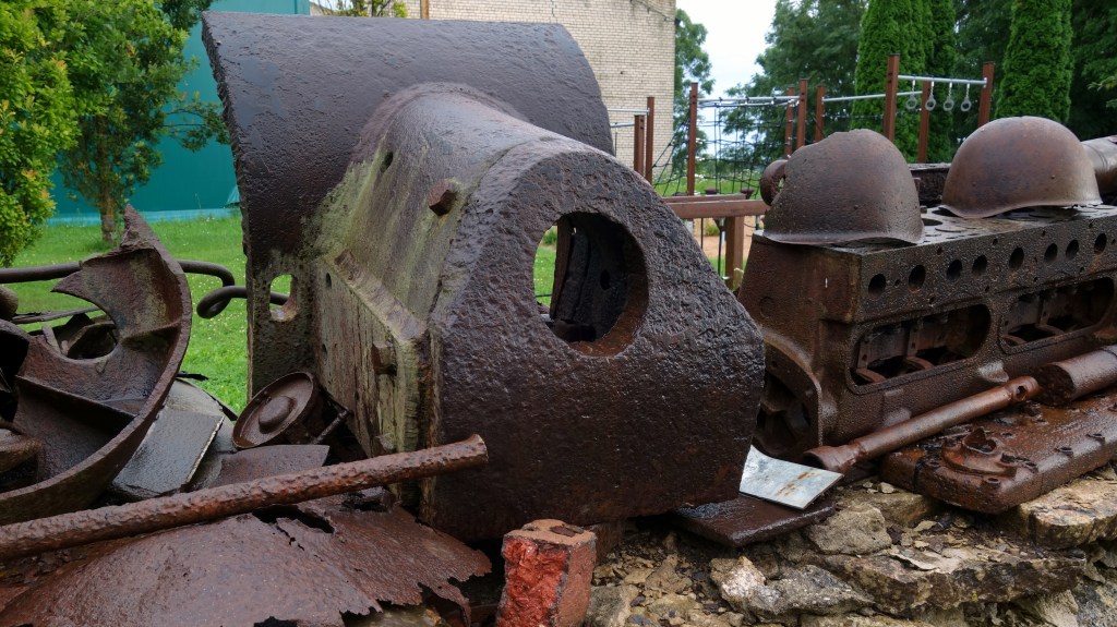 Kanonsmantel van een T34/76 naast twee russchische helmen op een muurtje naast het museum.